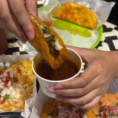 A birria taco being dipped into consommé